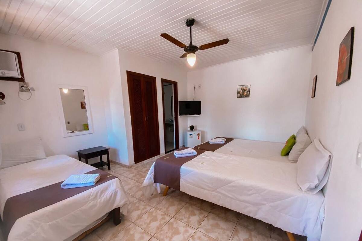 Ein Zimmer mit zwei Betten, einem Deckenventilator, einem Fernseher und einem kleinen Tisch.