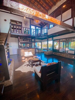 A spacious indoor area with a large pool, wooden furniture, and a stone accent wall. - Pousada Solar de Búzios (Búzios)