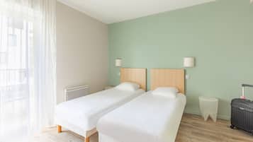 Ein Hotelzimmer mit zwei Einzelbetten, einem Nachttisch, einer Lampe, einem Heizkörper und einem Koffer.