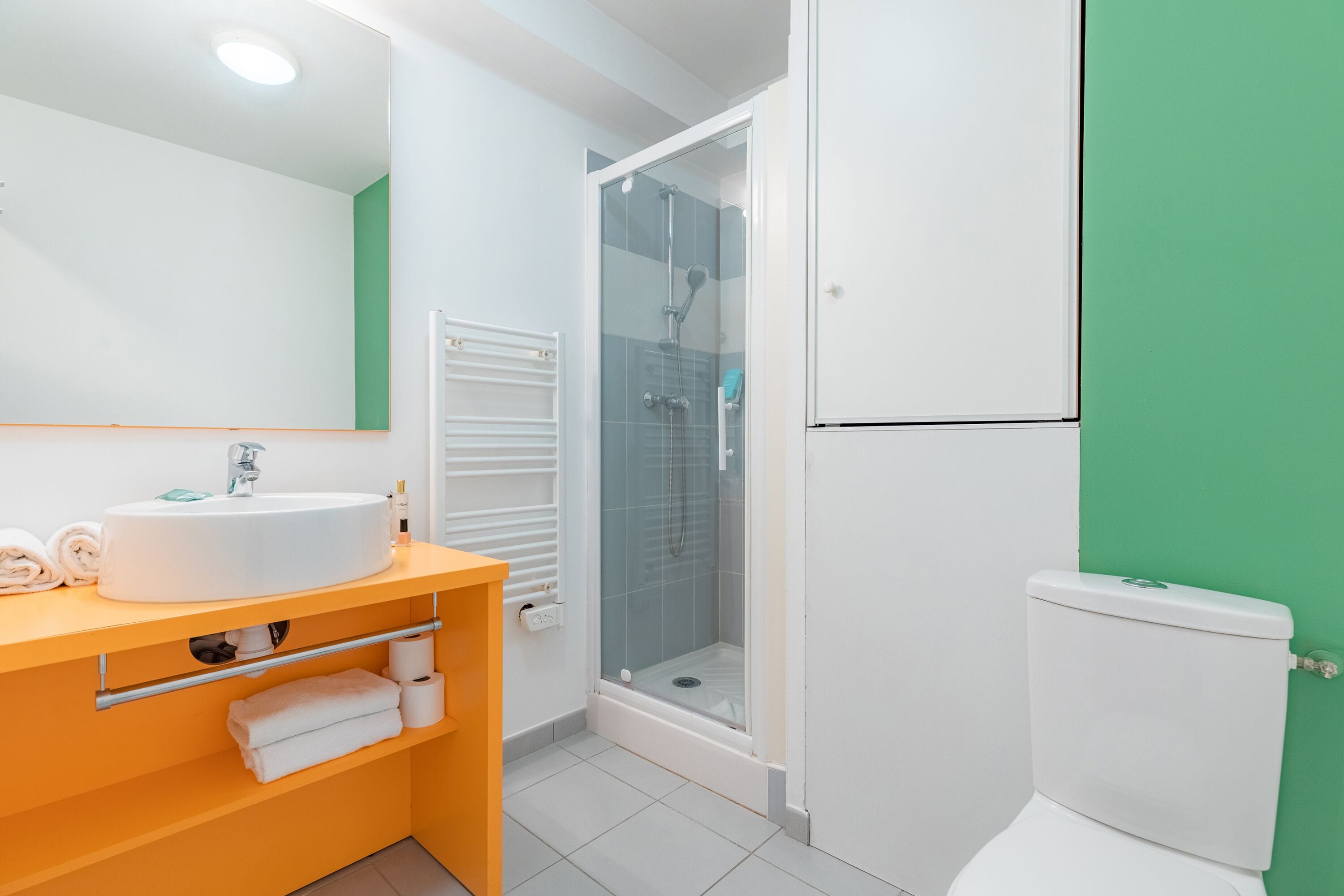 A bathroom with a white sink, mirror, and toilet, a glass-enclosed shower, and a green wall.