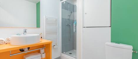 A bathroom with a white sink, mirror, and toilet, a glass-enclosed shower, and a green wall.