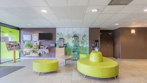 A reception area with a green wall, a reception desk, a seating area with yellow chairs, and a wall-mounted TV. - Appart'City Confort Tours (Tours)