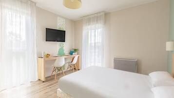 A hotel room with a bed, a desk with a chair, a television, and a radiator.