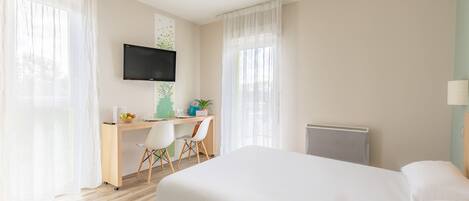 A hotel room with a bed, a desk with a chair, a television, and a radiator.