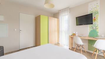 Ein modernes Hotelzimmer mit einem Bett, einem Schreibtisch mit Stühlen, einem Fernseher und einem Kleiderschrank.