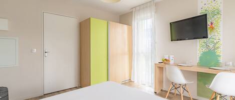 A modern hotel room with a bed, a desk with chairs, a television, and a wardrobe.