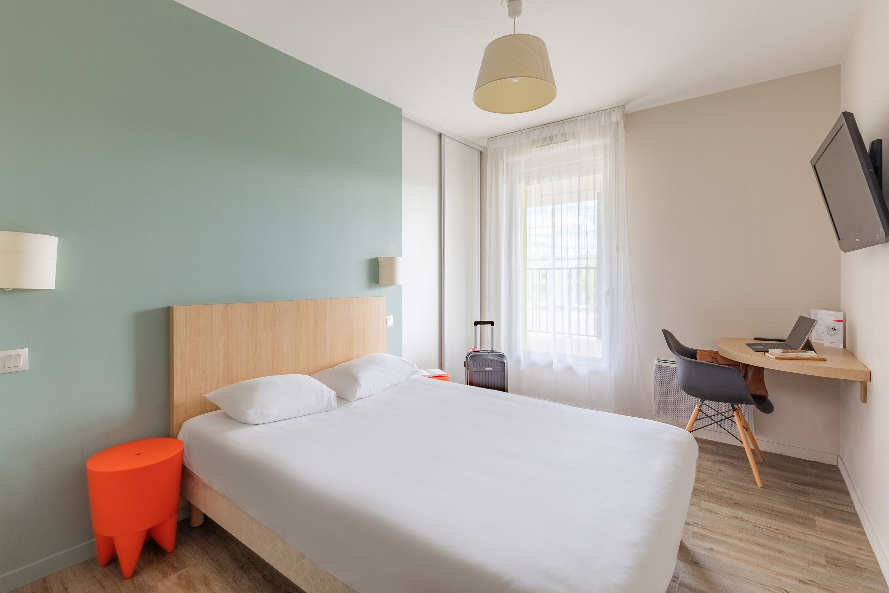 A hotel room with a bed, a desk, a chair, a suitcase, and a television.
