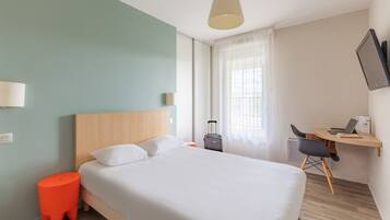 A hotel room with a bed, a desk, a chair, a suitcase, and a television.