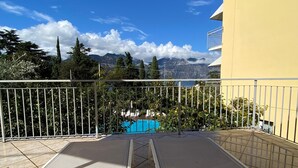 A balcony with a view of a swimming pool, a mountain range, and a yellow building. - Hotel Casa Serena (Malcesine)