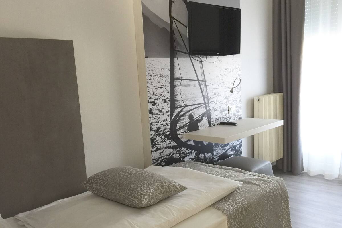 A hotel room with a bed, a mounted TV, a desk with a chair, and a window with curtains.