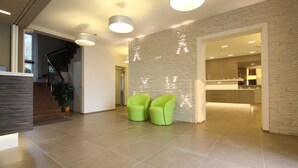 A spacious lobby with a modern staircase, a kitchen area, and two green chairs. - Hotel Casa Serena (Malcesine)