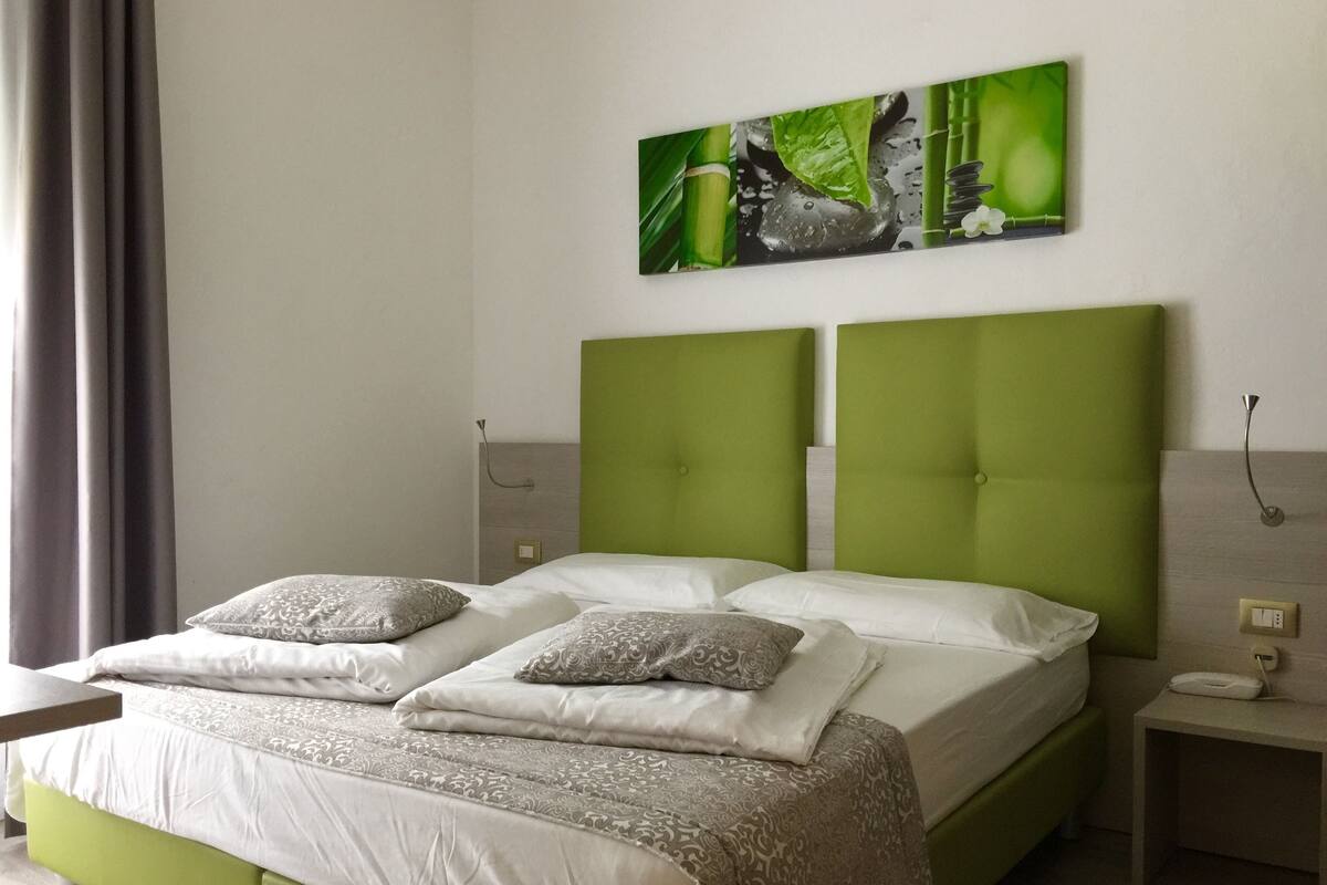 A double bed with green headboards, white bedding, and two decorative pillows.