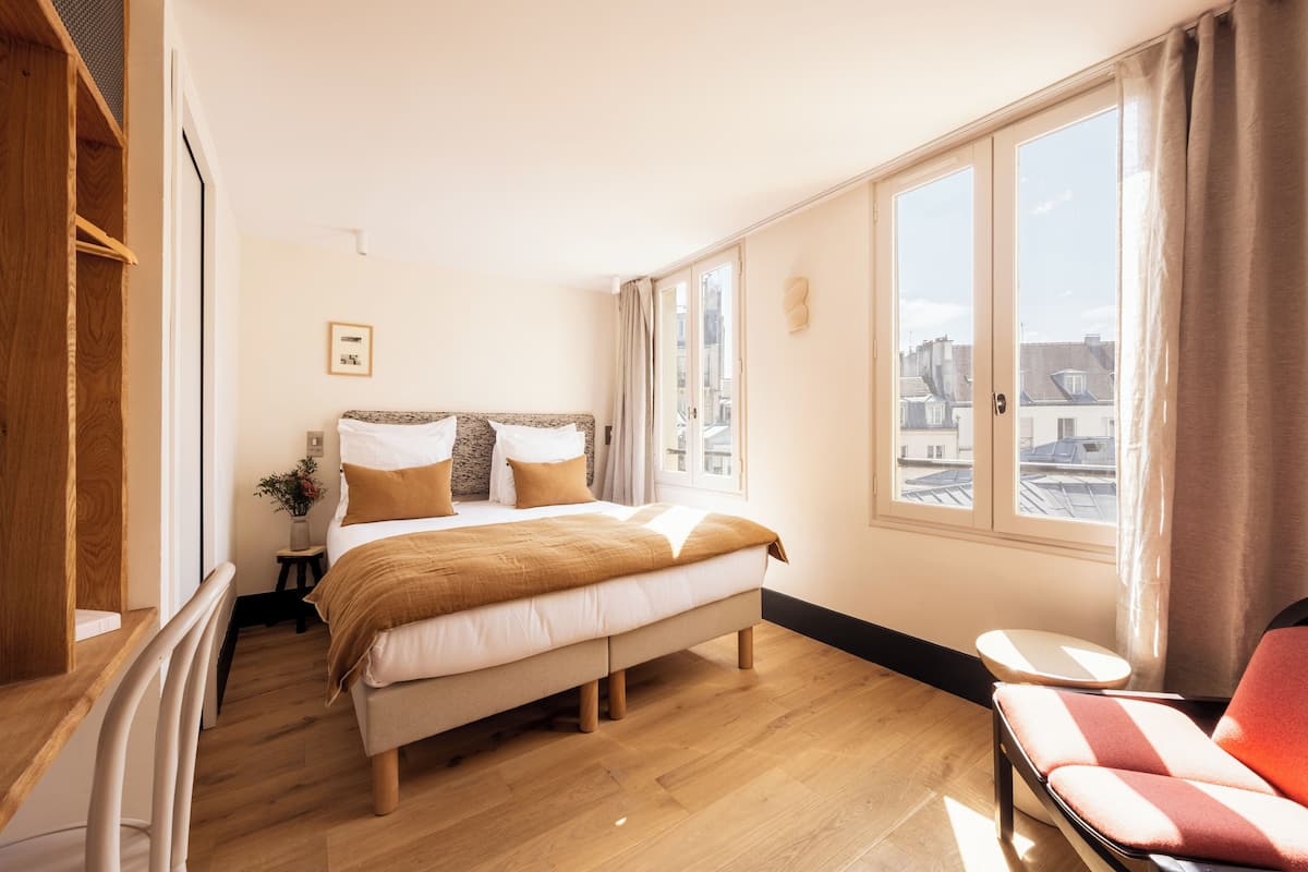 A bedroom with a bed, a chair, a small table, and a window with a city view.