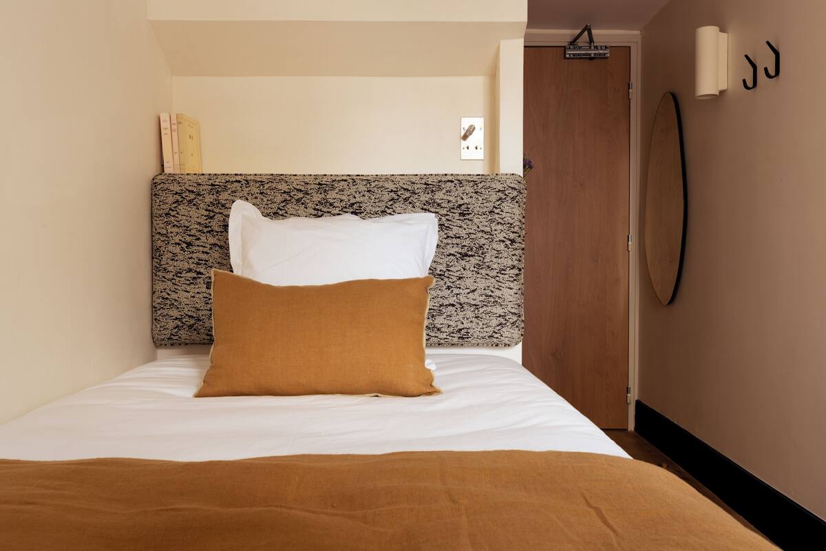 A neatly made bed with white and brown bedding, a patterned headboard, and a wooden door in the background.