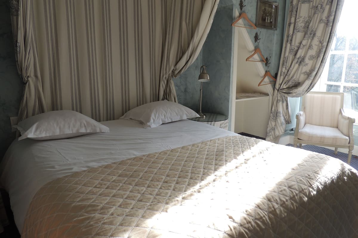 Un lit avec une couette, une table de chevet, une lampe, une chaise et des rideaux.