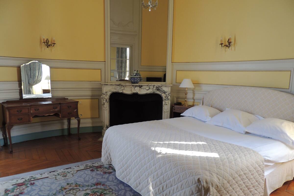 Une chambre à coucher avec un grand lit, une commode, un miroir, une cheminée et un tapis à motifs floraux.