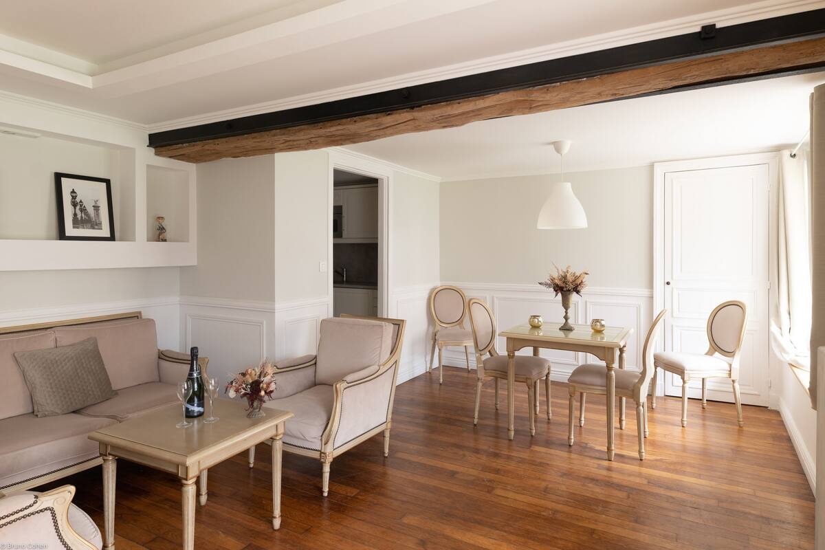 Un salon avec un plancher en bois, un canapé, une table basse avec une bouteille et des verres, et un coin repas avec des chaises et une table.