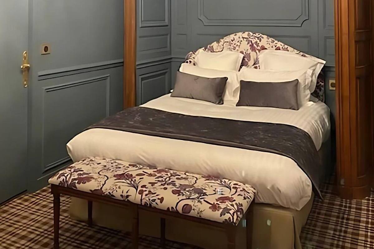 Une chambre avec un grand lit, un banc, un lustre et un mur bleu.