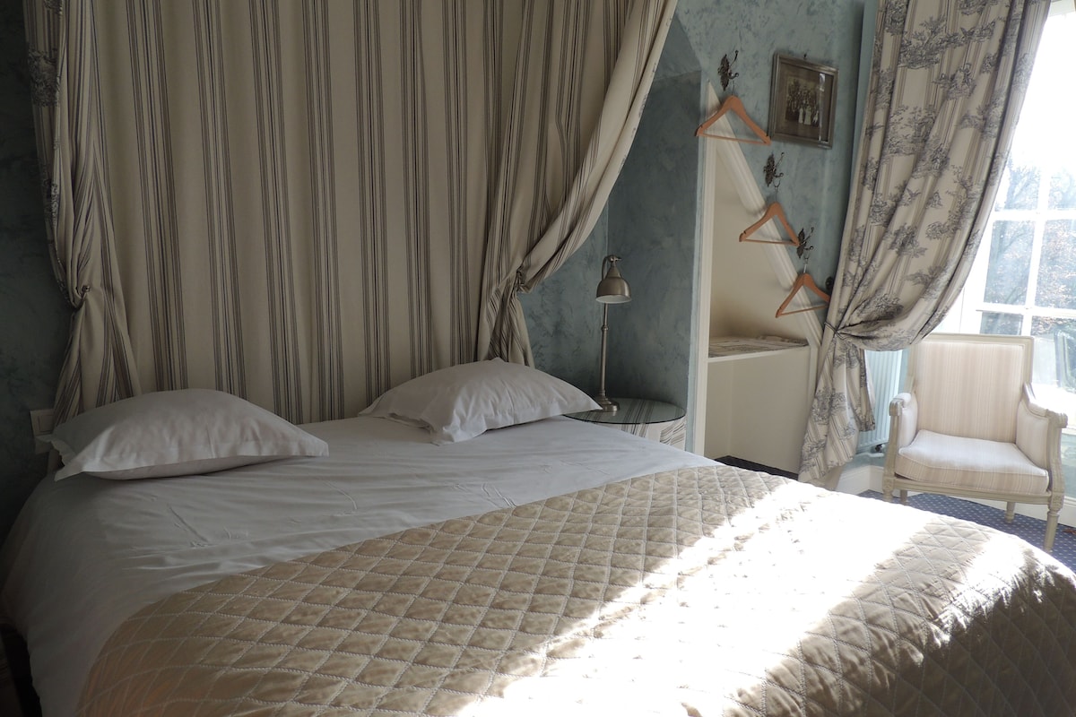 A bed with a quilt, a nightstand, a lamp, a chair, and curtains.