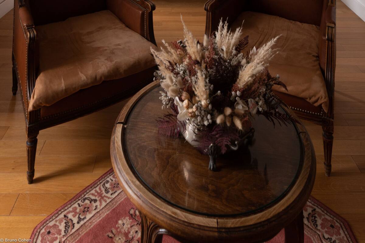 Une chambre à coucher comprenant un lit, deux fauteuils, une table de chevet, une lampe et un vase décoratif posé sur une table.