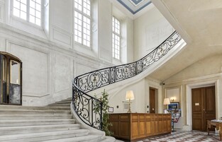 Una imponente escalera con barandillas negras ricamente decoradas, un mostrador de recepción de madera y un suelo a cuadros.