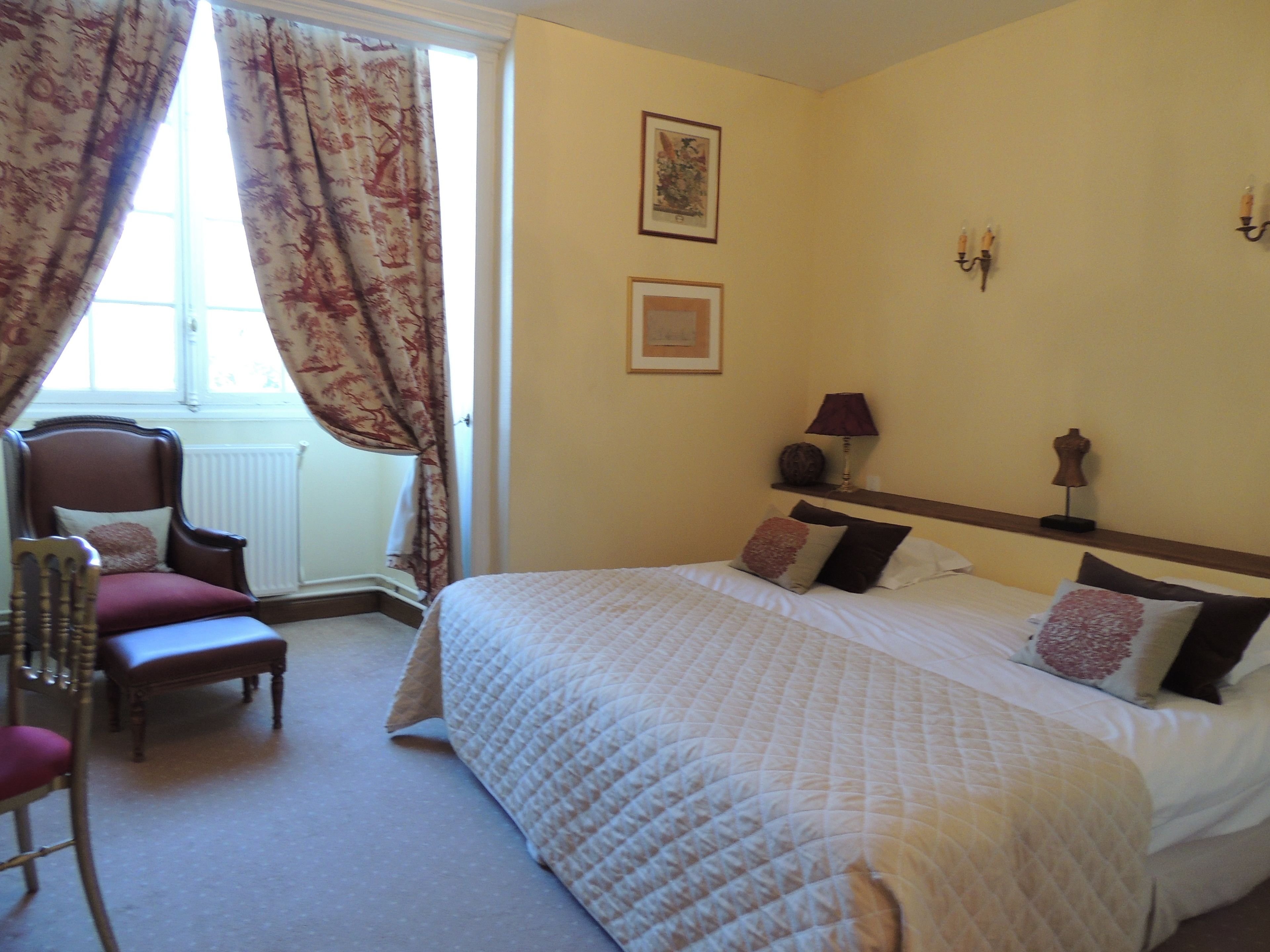 Habitación de hotel con una cama grande, una silla, ventana con cortinas, una lámpara y decoración en la pared.
