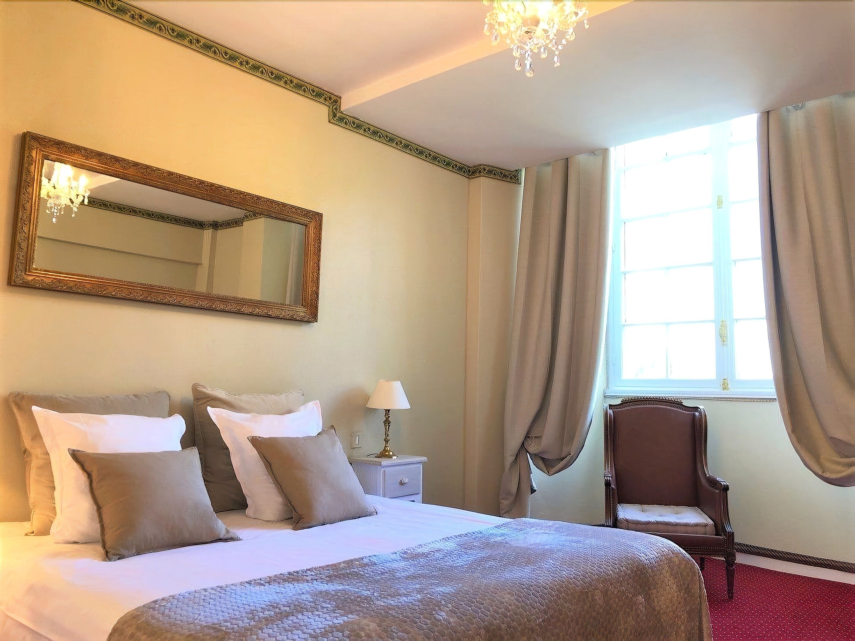 Una habitación de hotel con una cama grande, un espejo, una silla y un ventanal con cortinas.