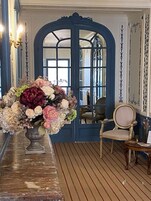 Una habitación con una puerta azul grande, suelo de madera y un jarrón de flores sobre una mesa.