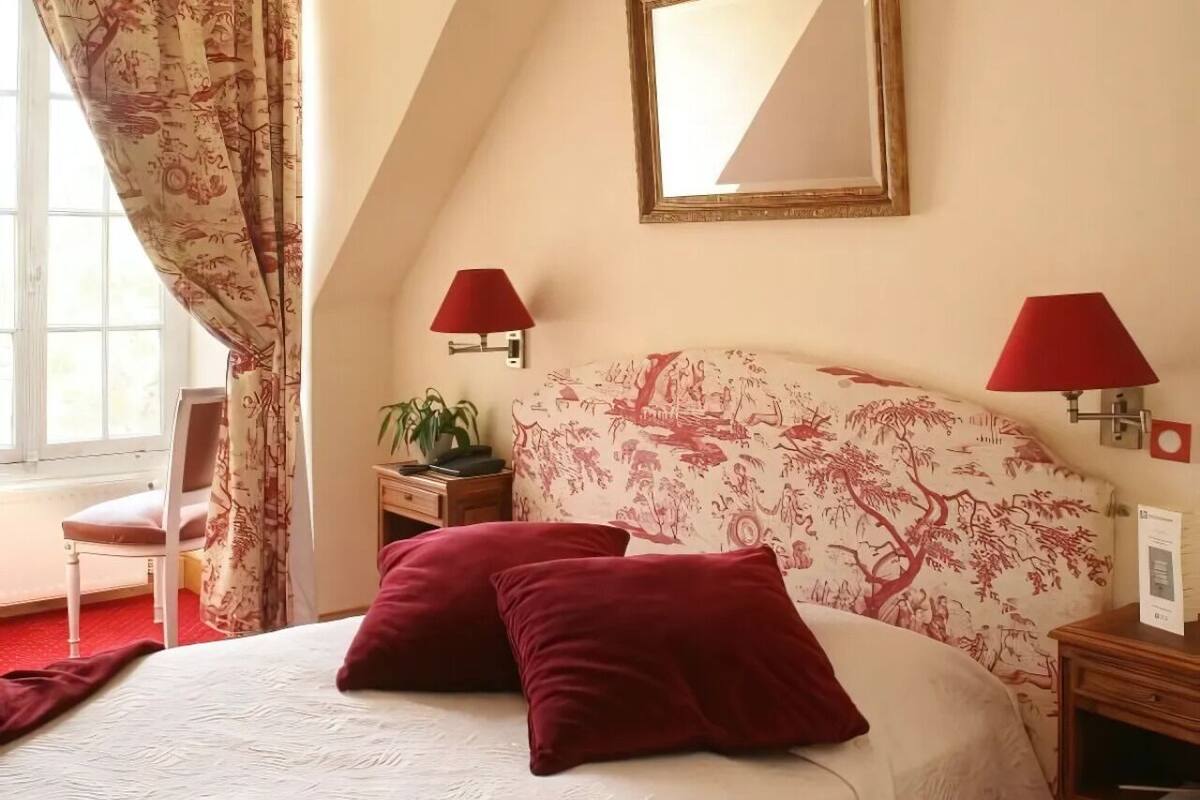 Une chambre à coucher avec un lit, deux lampes rouges, un miroir et une fenêtre avec des rideaux.