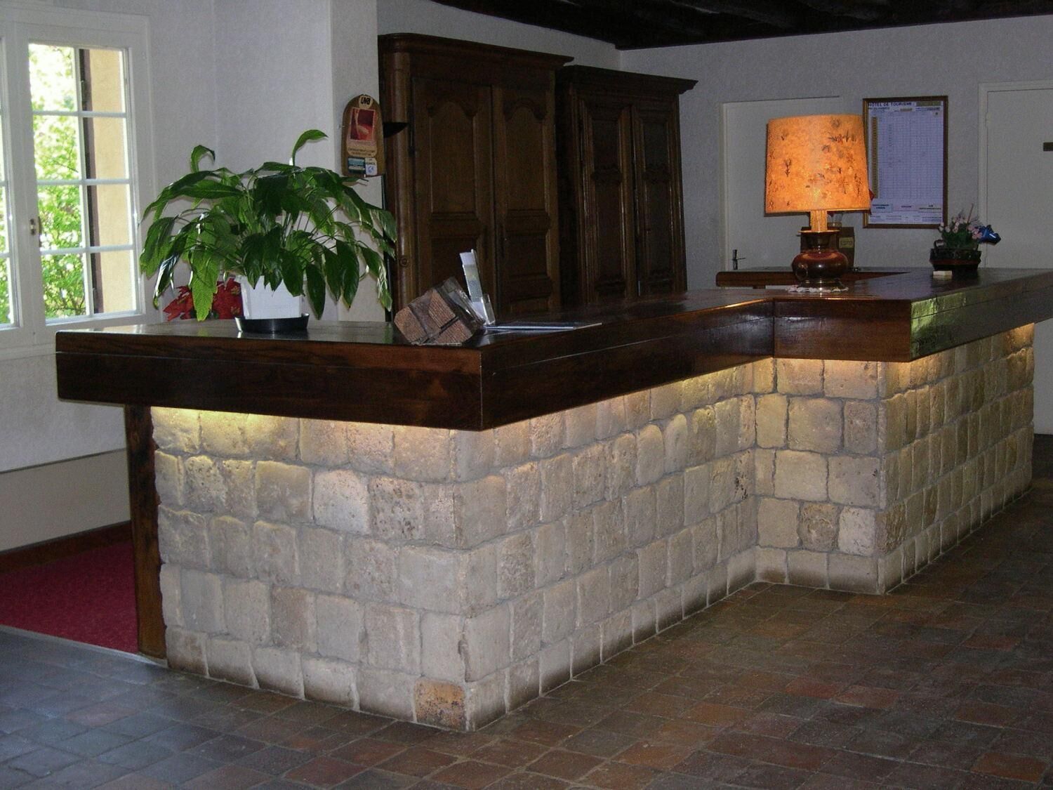 Zona de recepción con mostrador de piedra, una planta en maceta, un armario de madera y una lámpara.