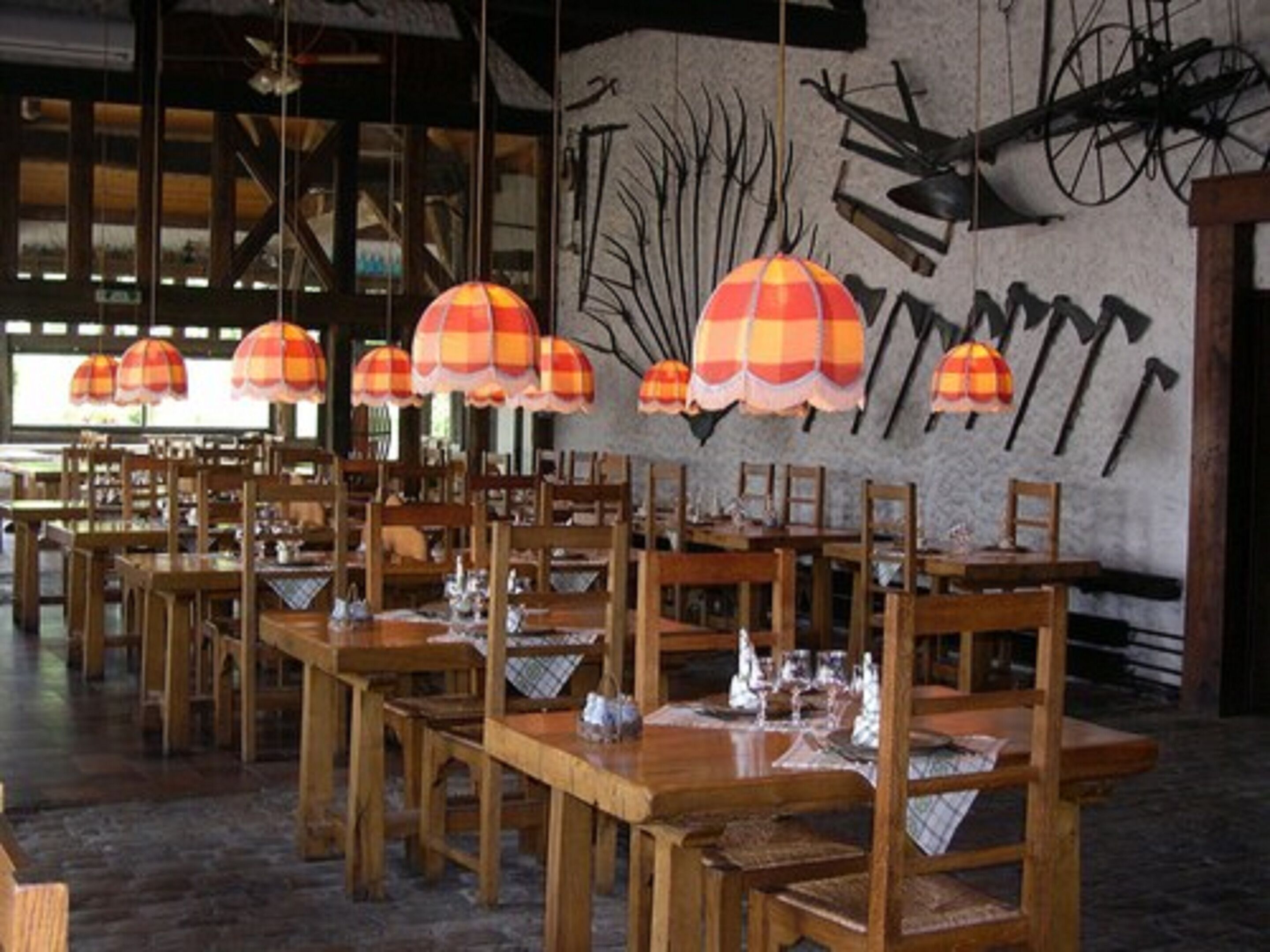 Restaurante com mesas e cadeiras de madeira, luminárias listradas em laranja e branco, e uma parede com bicicletas penduradas.