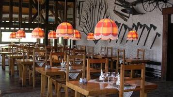 Restaurante com mesas e cadeiras de madeira, luminárias listradas em laranja e branco, e uma parede com bicicletas penduradas.