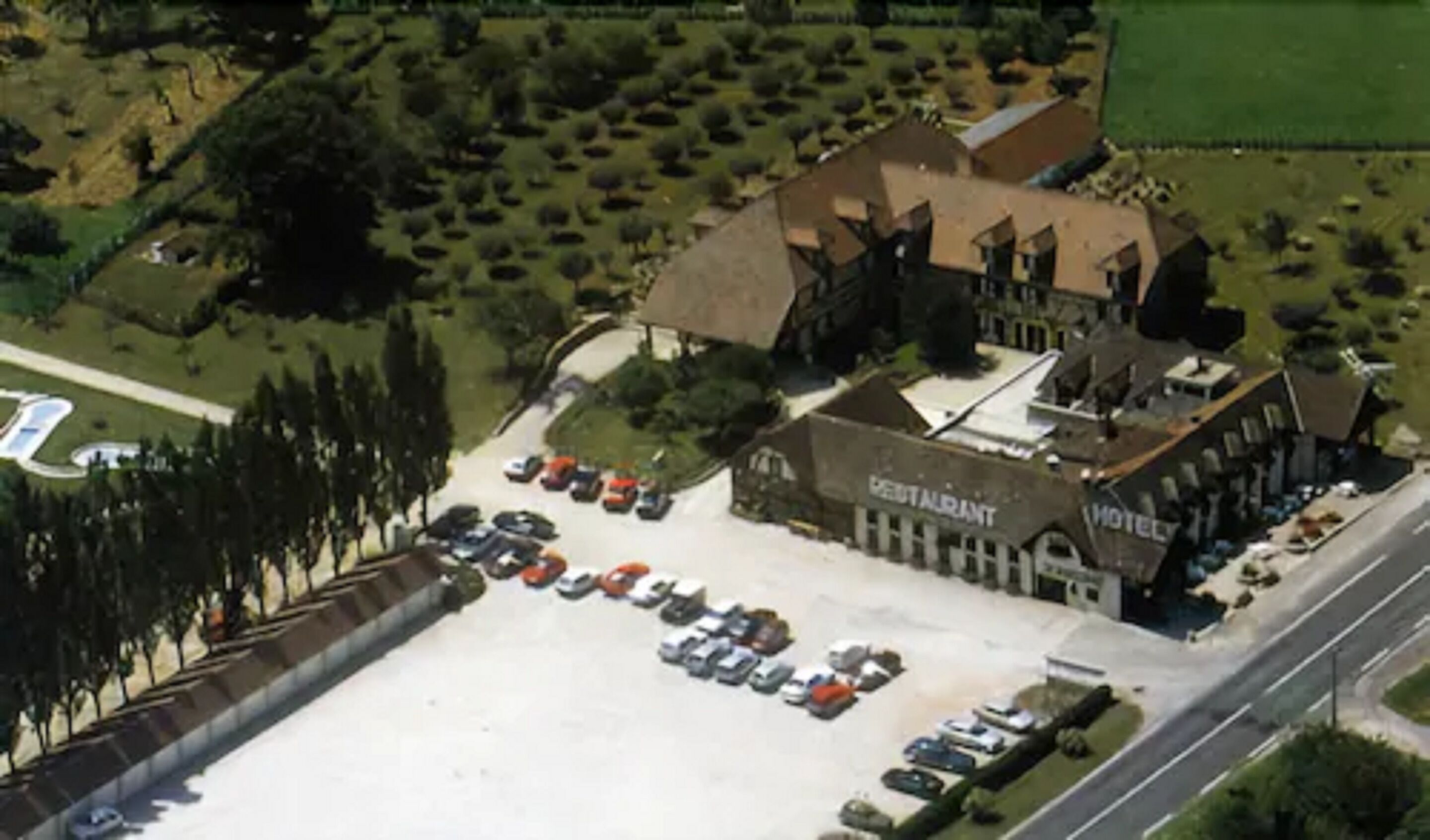 An aerial view of a hotel with a large parking lot, a restaurant, and a hotel building.
