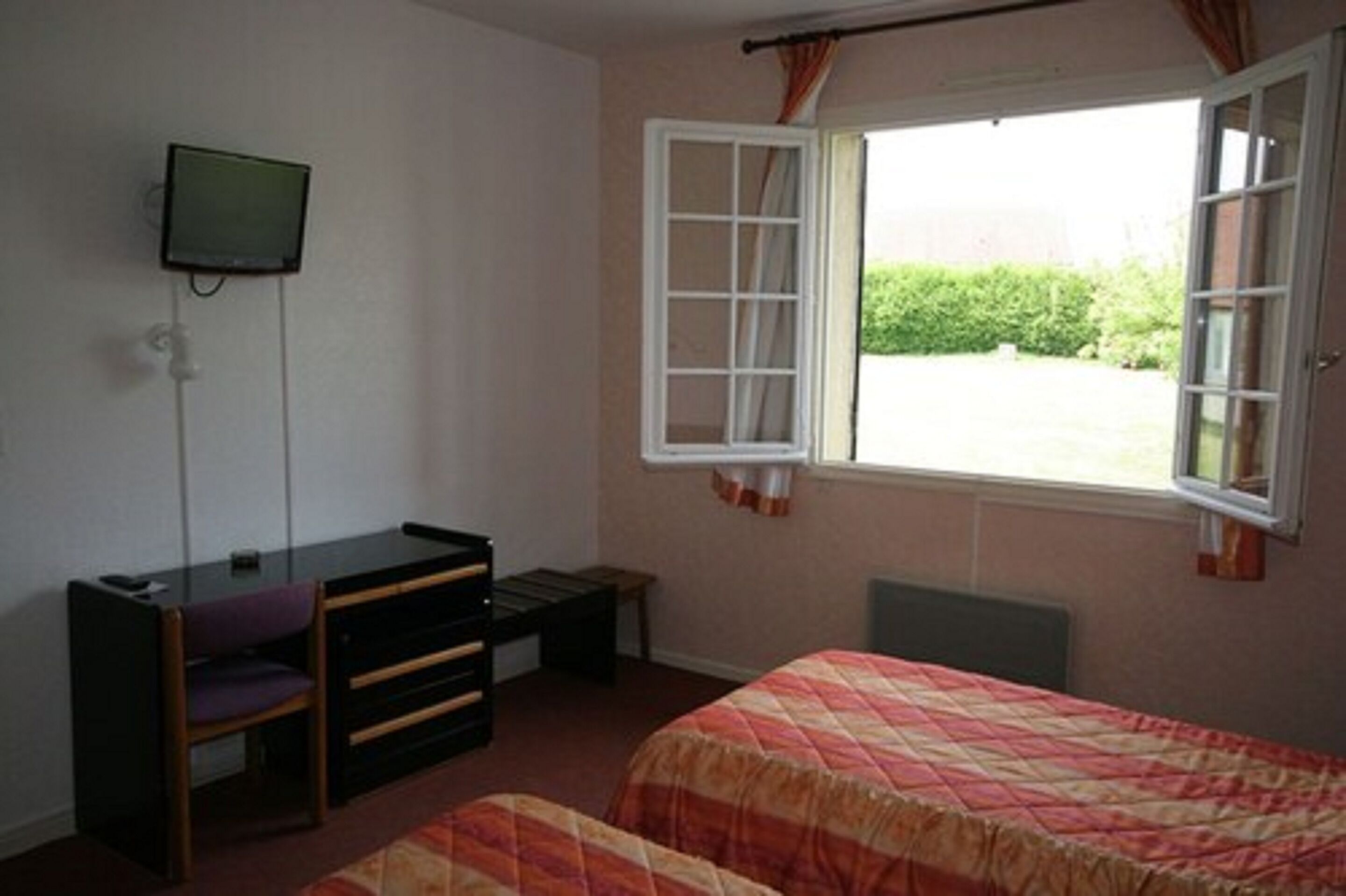Un dormitorio con cama, escritorio, silla, televisor y ventana.