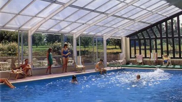 An indoor swimming pool with a glass ceiling, surrounded by lounge chairs and a view of greenery outside. - Hôtel Restaurant La Mangeoire – Relais Paris Bâle (Montieramey)