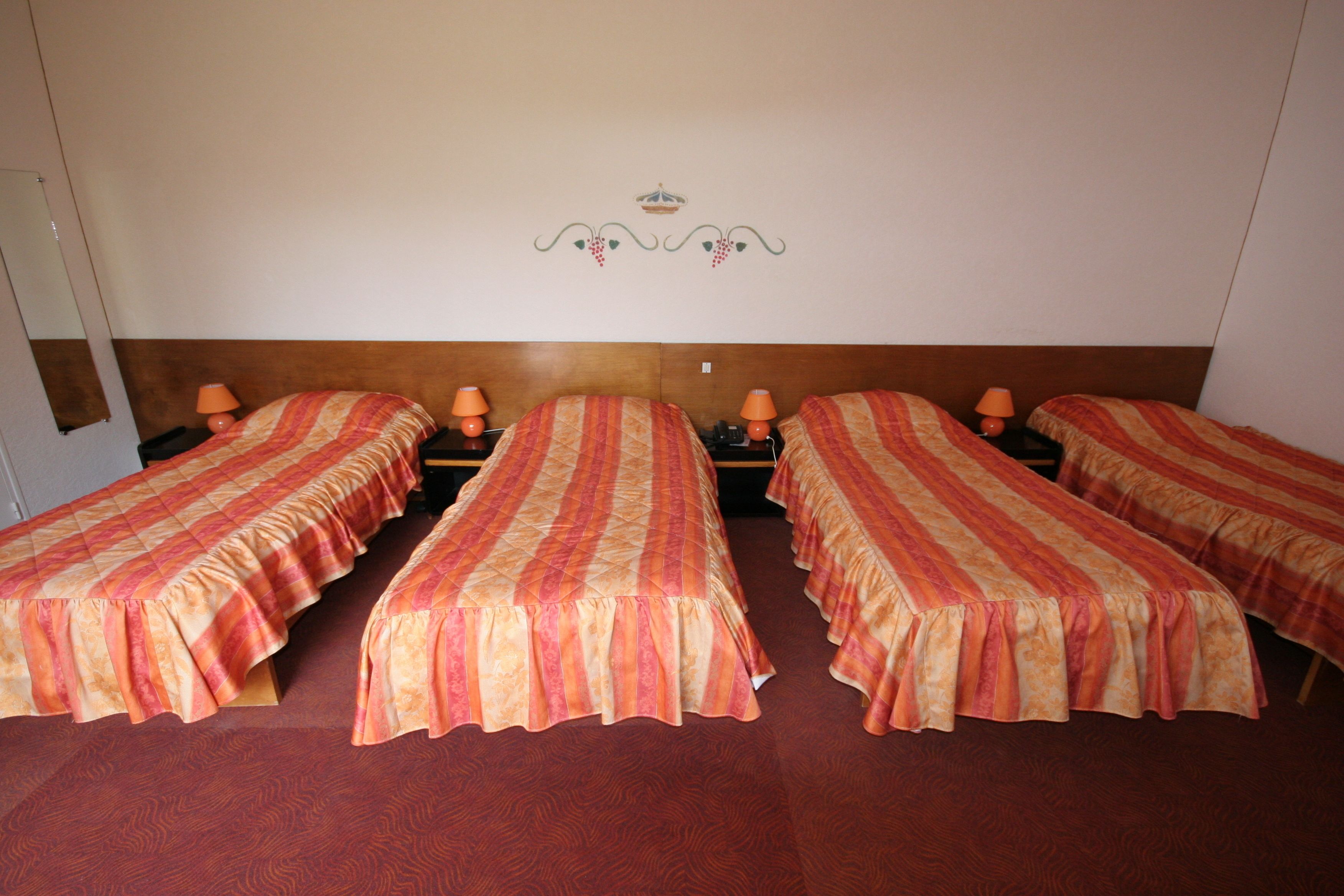 Une chambre d’hôtel avec trois lits simples, chacun recouvert d’une couvre-lit à rayures et agrémenté d’une lampe orange placée à côté.