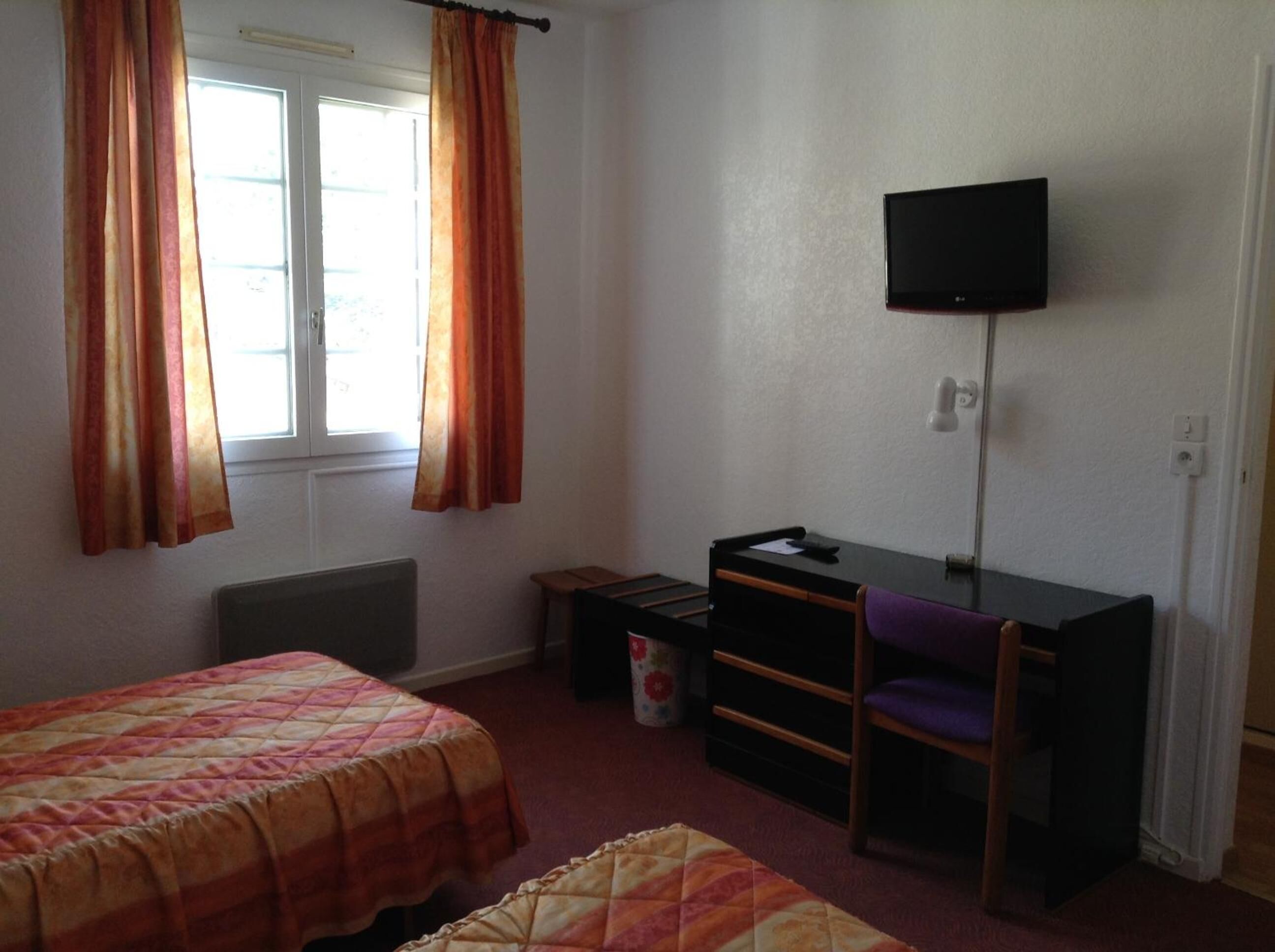 A room with two beds, a desk, a chair, a television, and a radiator.