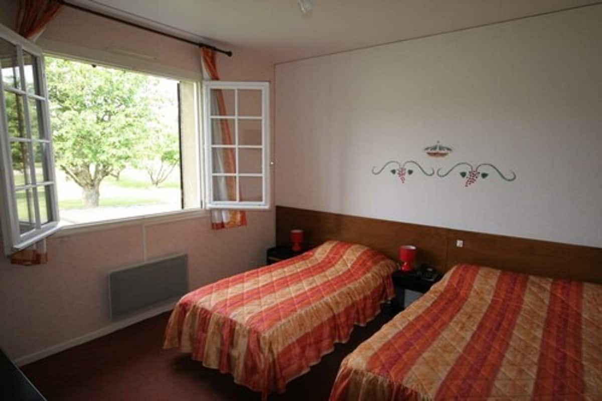 Une chambre avec deux lits, une fenêtre avec des rideaux, un radiateur et un élément décoratif mural.