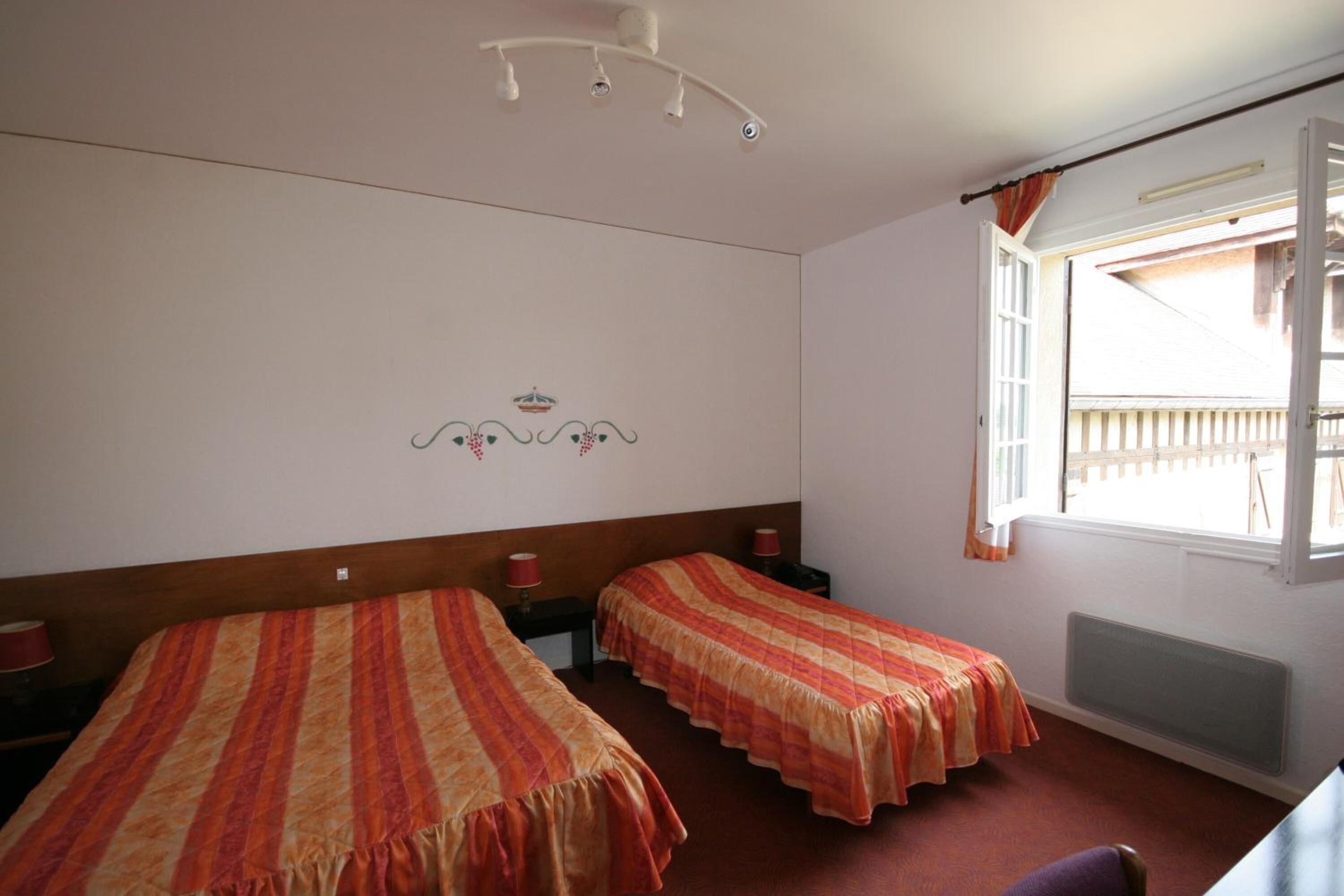 Una habitación con dos camas individuales, una ventana con cortinas, un adorno en la pared y una lámpara en el techo.