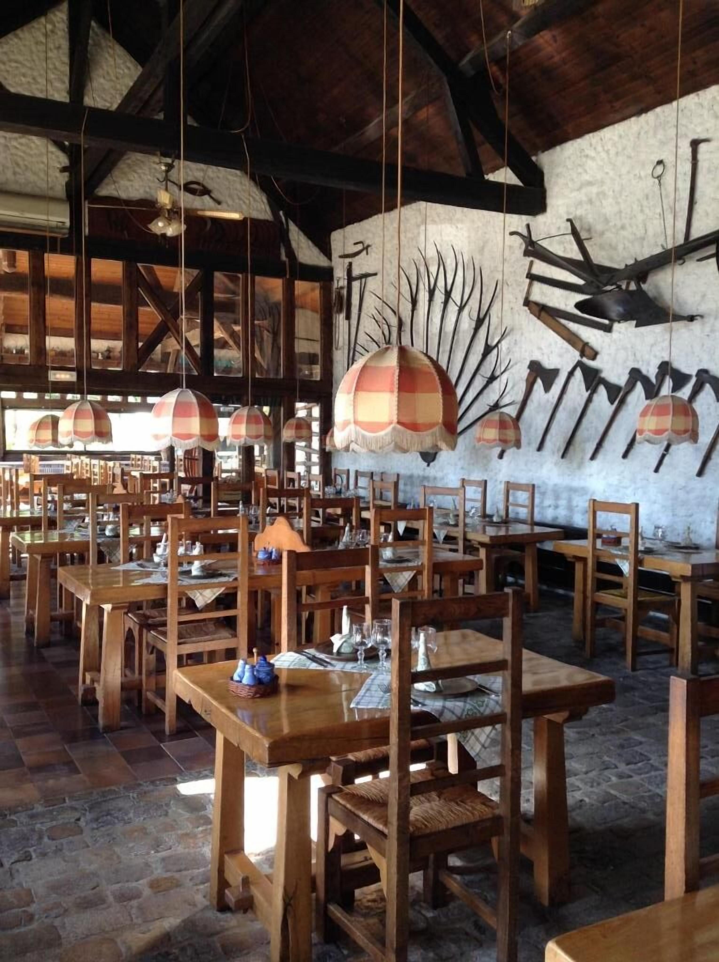 A rustic dining area with wooden tables and chairs, hanging lamps, and a wall decorated with antlers and other rustic items.