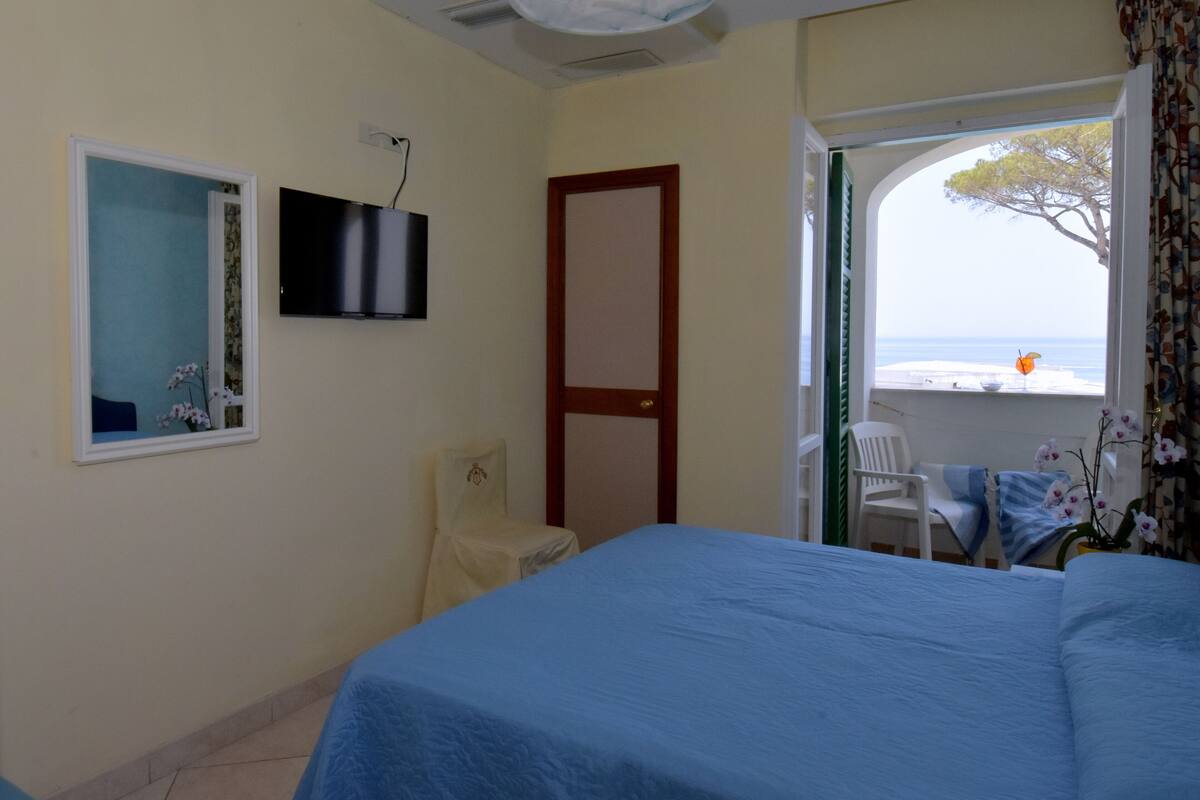 Un dormitorio con cama, una silla, televisor y ventana con vista al mar.