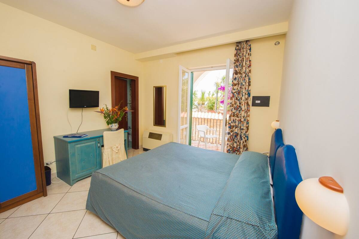 Un dormitorio con cama, televisión, escritorio y ventana con vistas al exterior.