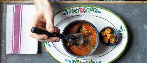 A person serving a bowl of soup with a spoon on a decorative plate.