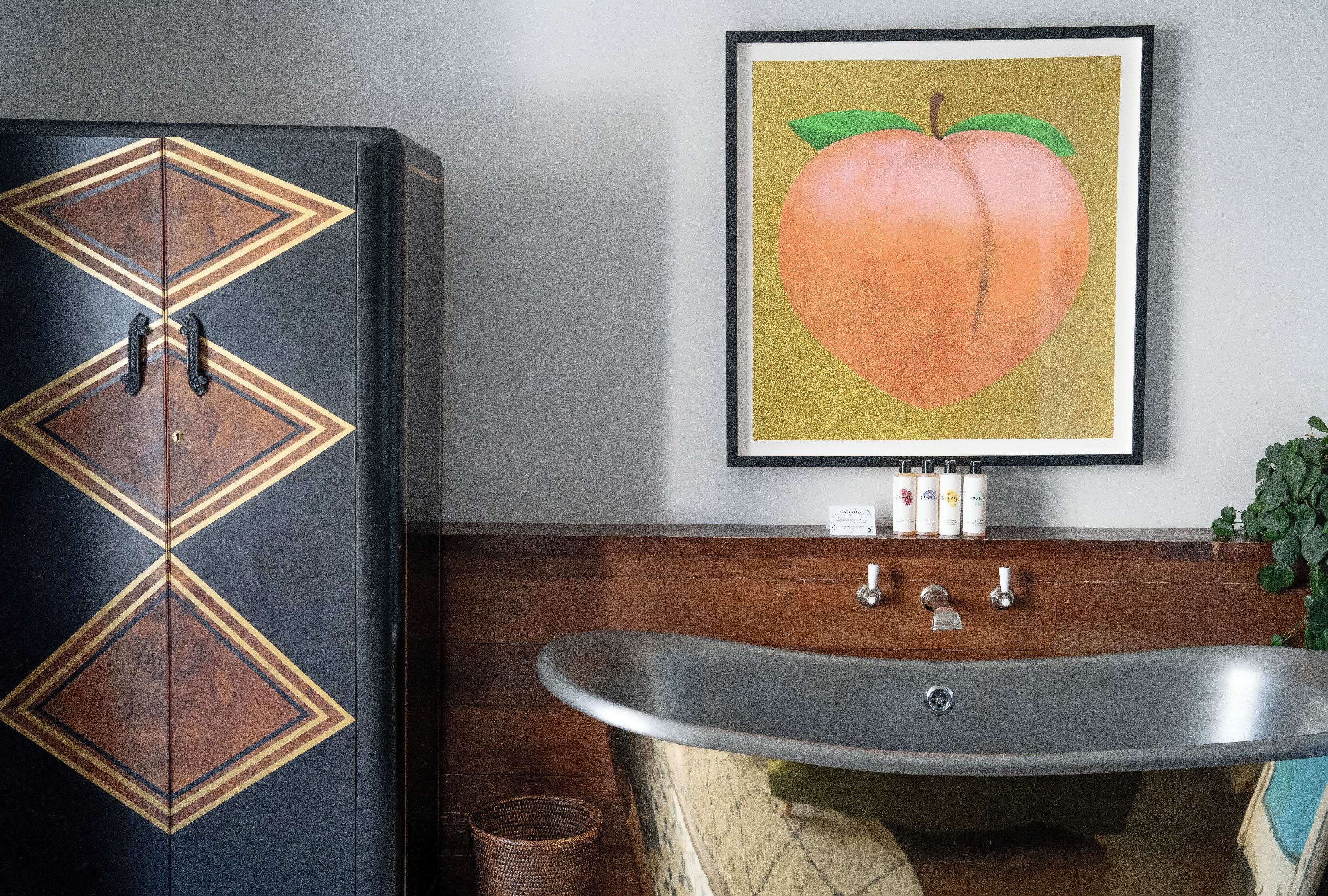 Un baño con una bañera antigua, un mueble de madera con diseños geométricos y un cuadro con un pez melocotón en la pared.