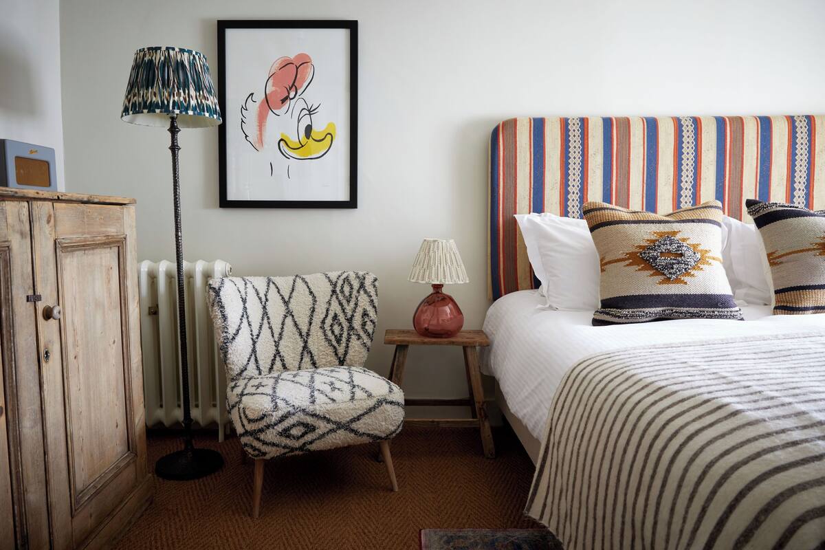 A bedroom with a striped headboard, a patterned armchair, a radiator, and a framed picture on the wall.
