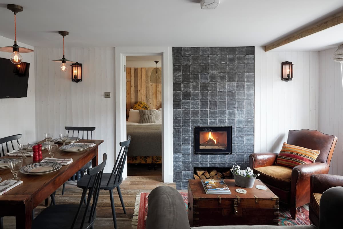A cozy living room with a fireplace, wooden dining table set for four, and comfortable seating.