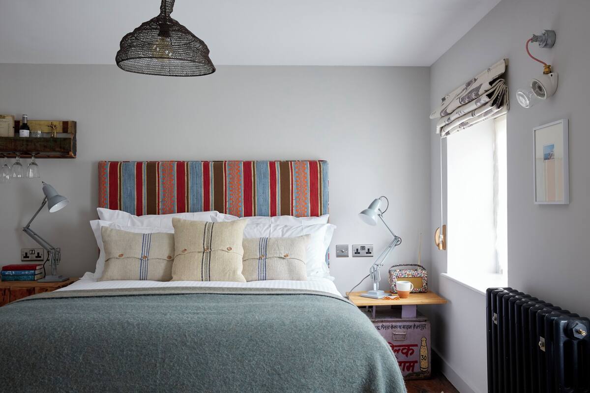 A neatly arranged bedroom with a bed, bedside lamps, a radiator, and a window with curtains.