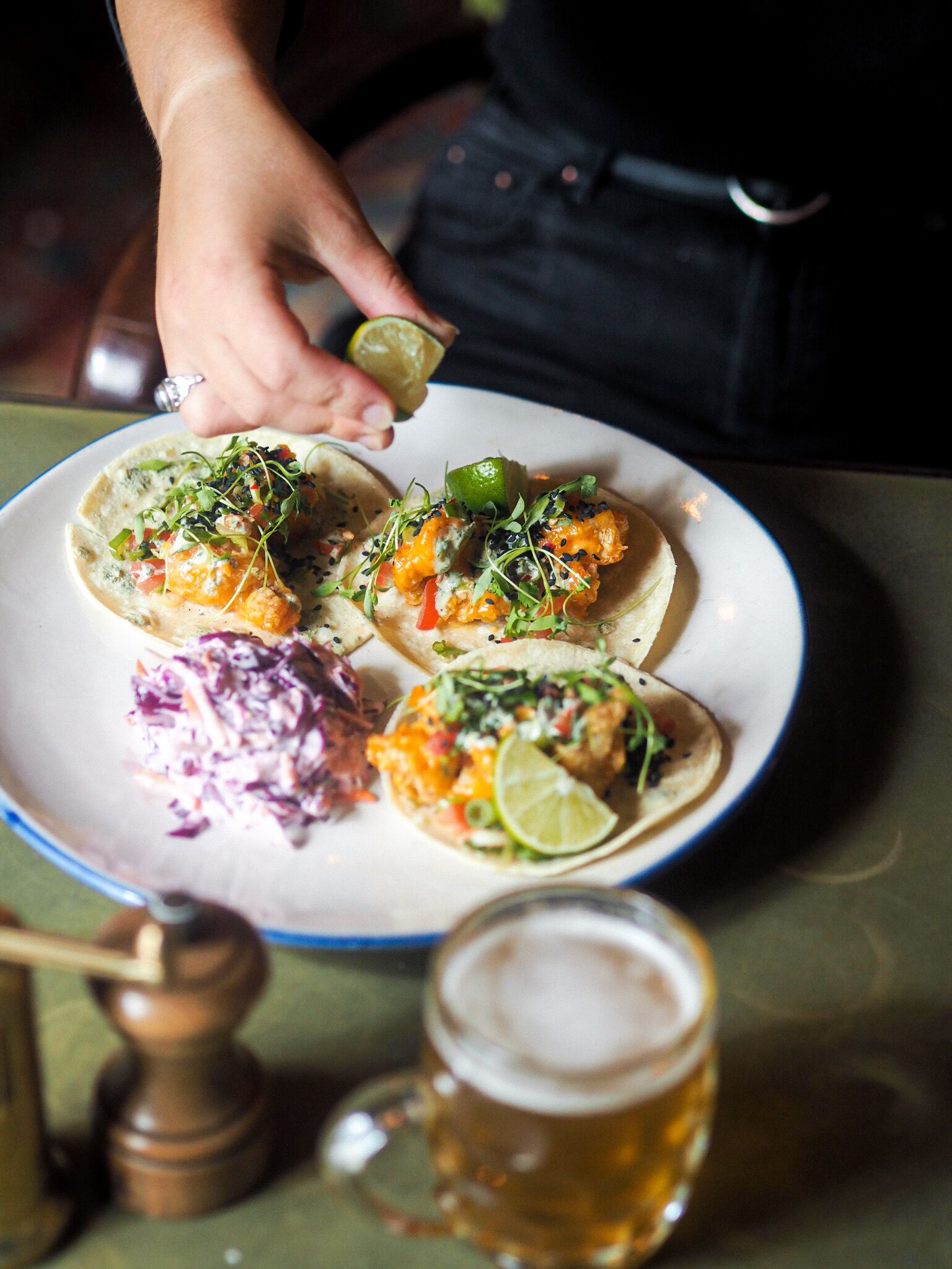 A plate of tacos with lime wedges and a side of coleslaw, accompanied by a beer mug.
