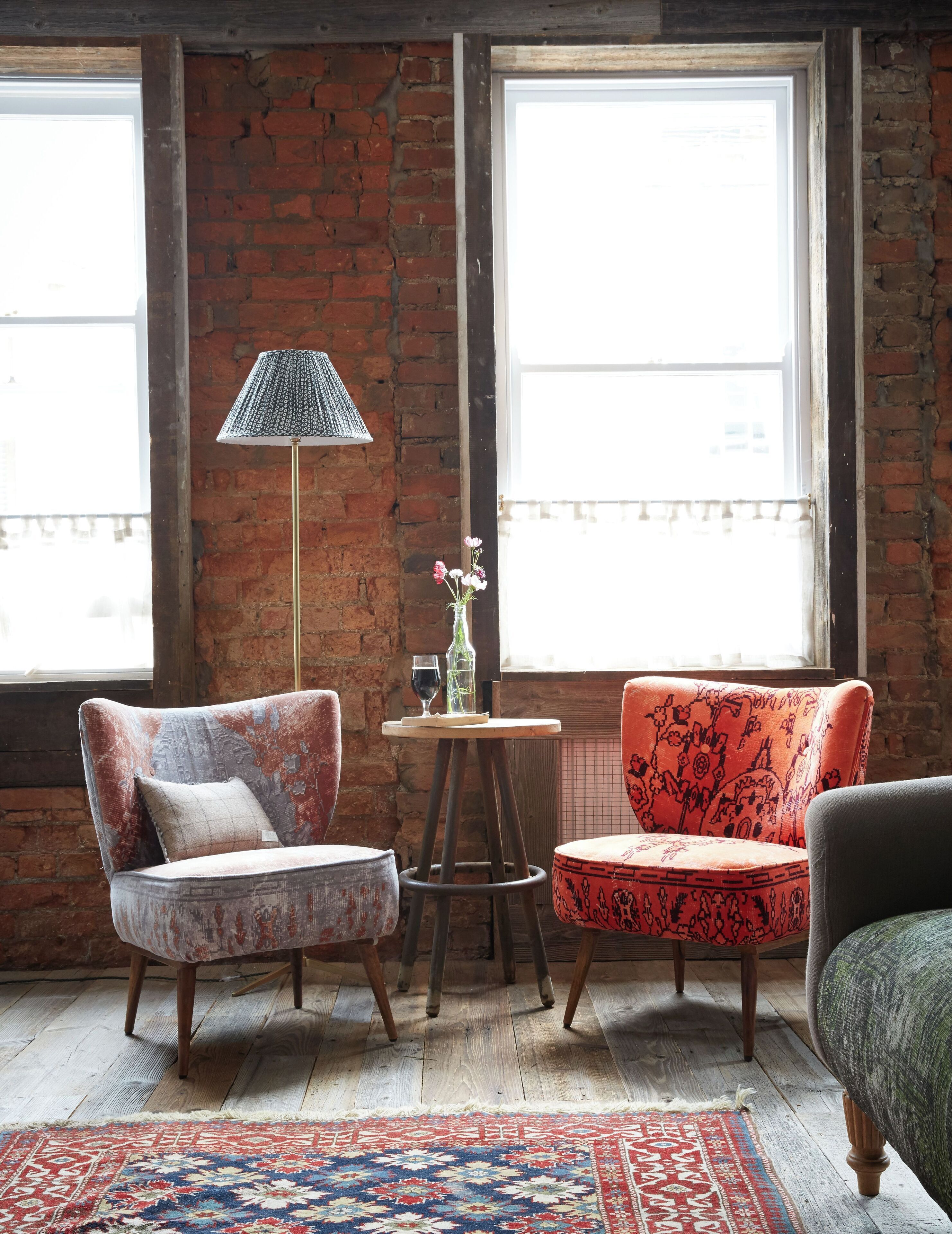 A cozy room with two vintage armchairs, a small table with a vase of flowers, and a floor lamp.