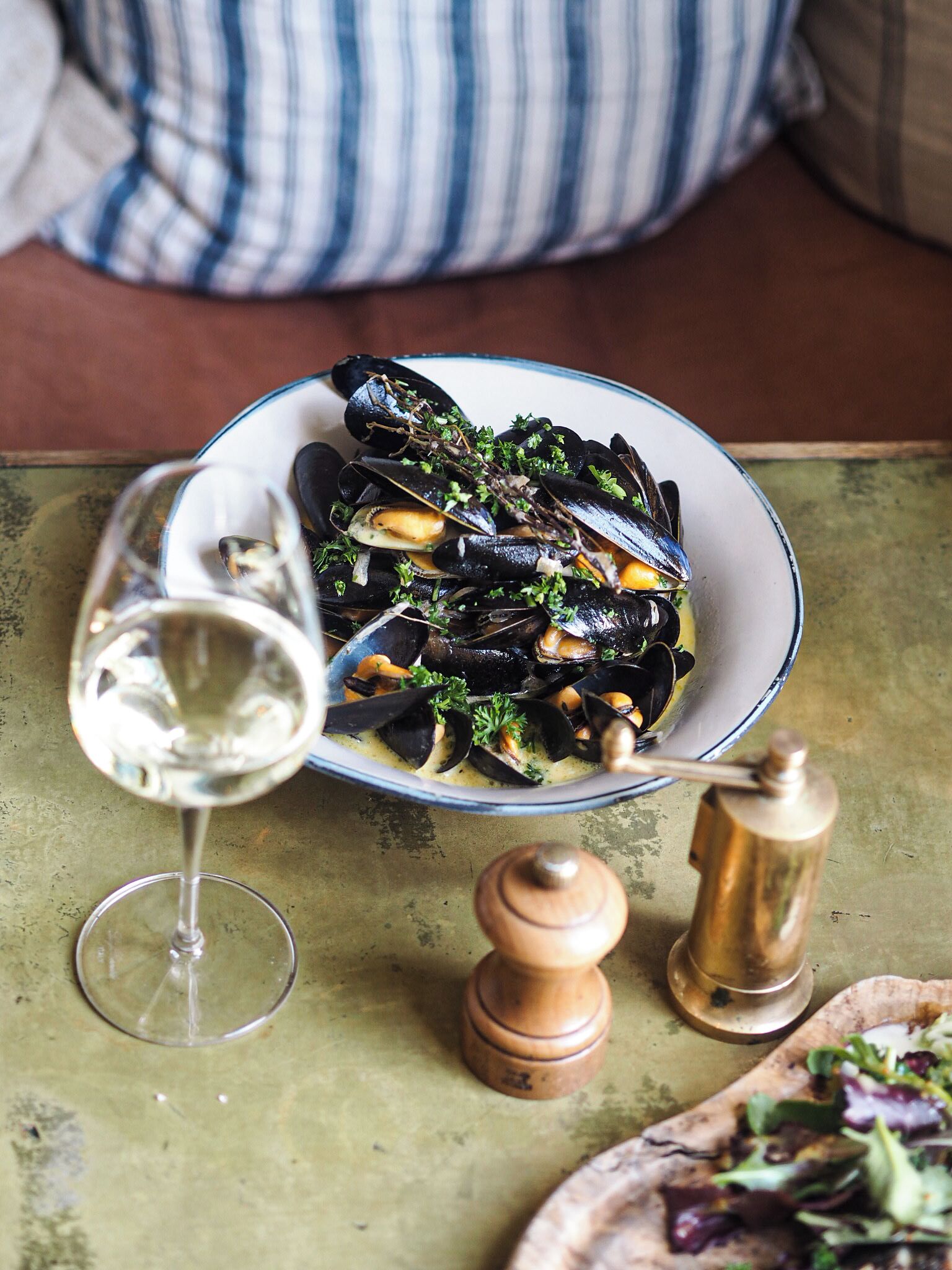 Un plato de mejillones con una copa de vino blanco y un molinillo de pimienta sobre una mesa.